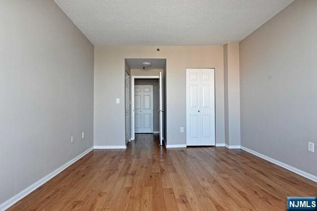 interior space with wood finished floors, baseboards, a closet, and a textured ceiling