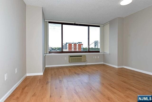 unfurnished room with an AC wall unit, baseboards, light wood-type flooring, and a wealth of natural light