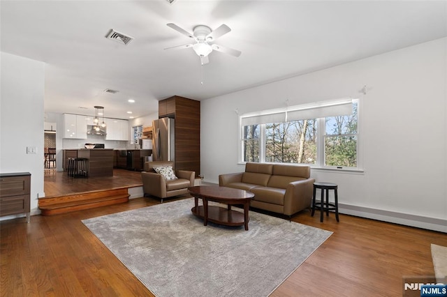 living area with a ceiling fan, recessed lighting, wood finished floors, and visible vents