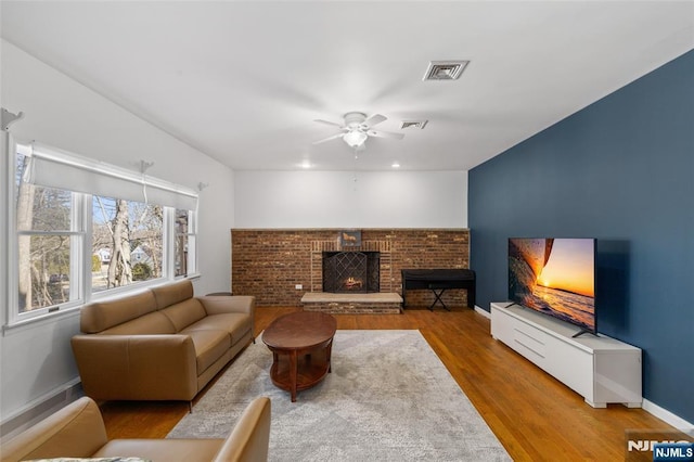 living room with a brick fireplace, wood finished floors, visible vents, and baseboards