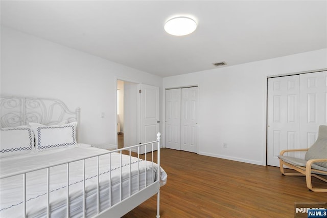 bedroom with visible vents, baseboards, two closets, and wood finished floors