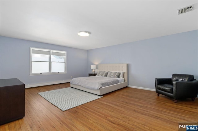 bedroom with visible vents, light wood-type flooring, baseboards, and a baseboard radiator