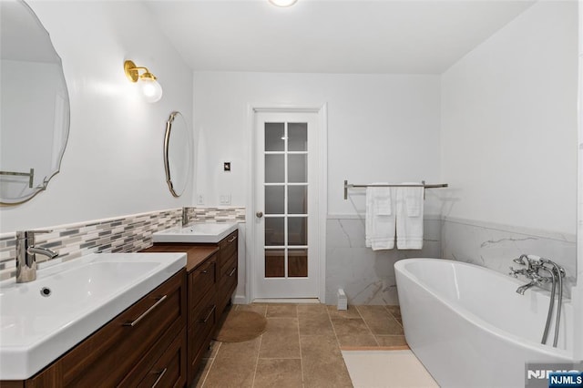 bathroom with two vanities, wainscoting, a freestanding tub, tile walls, and a sink