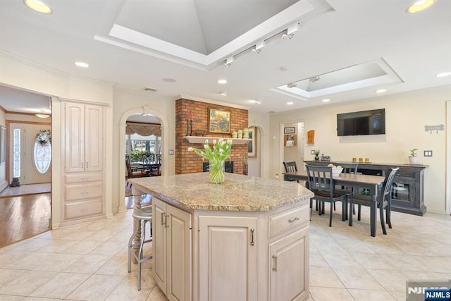 kitchen with a raised ceiling, arched walkways, a fireplace, and a kitchen island