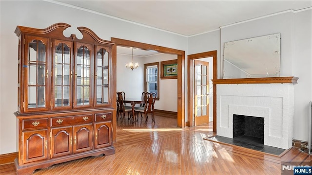 interior space with baseboards, light wood-style flooring, ornamental molding, an inviting chandelier, and a fireplace