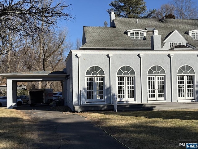 view of property exterior with an attached carport, roof with shingles, stucco siding, a chimney, and french doors