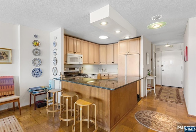 kitchen featuring white microwave, a peninsula, a breakfast bar, stainless steel gas stove, and dark stone countertops