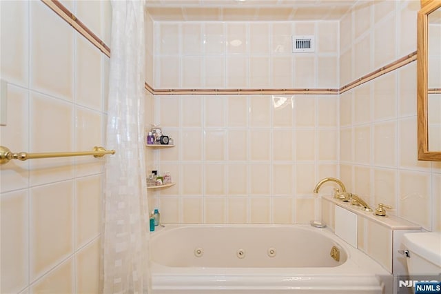 bathroom featuring visible vents, toilet, tile walls, and a whirlpool tub