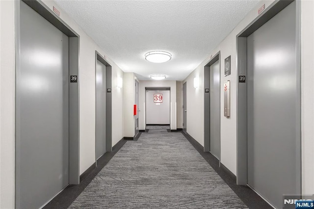 corridor with elevator, baseboards, dark carpet, and a textured ceiling