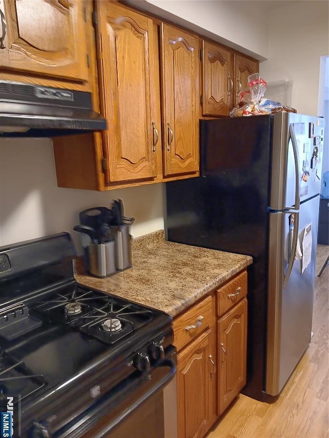 kitchen with brown cabinets, light wood finished floors, black gas range, and under cabinet range hood