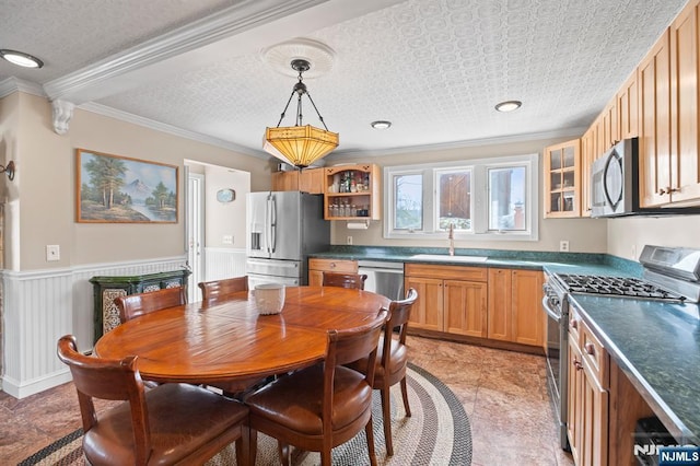 interior space featuring a wainscoted wall, a sink, appliances with stainless steel finishes, ornamental molding, and dark countertops