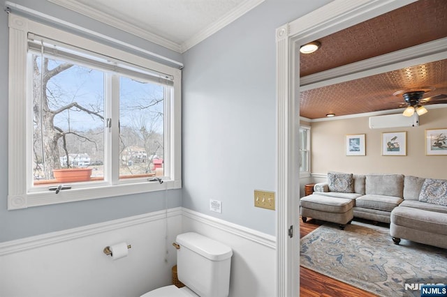 bathroom with a wainscoted wall, crown molding, toilet, a ceiling fan, and wood finished floors