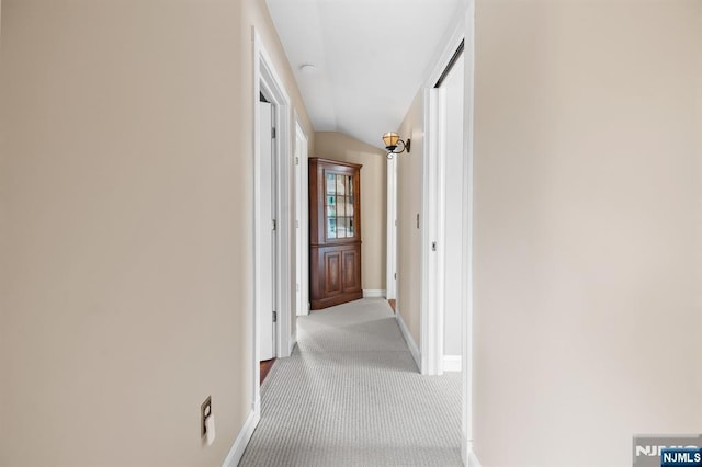 corridor with carpet, baseboards, and vaulted ceiling