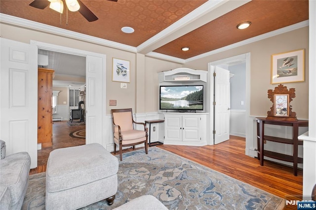 living room with a wainscoted wall, ceiling fan, crown molding, and wood finished floors