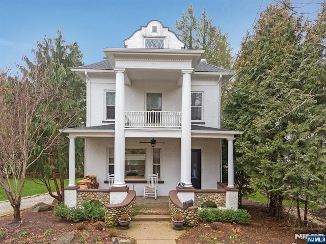 neoclassical / greek revival house featuring a shingled roof, a balcony, ceiling fan, a porch, and stucco siding