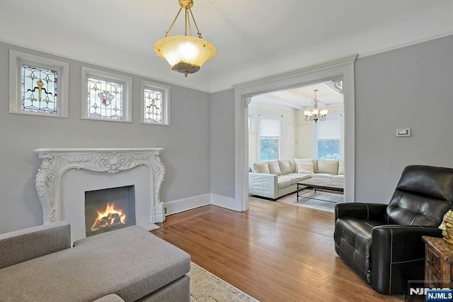 living room featuring a chandelier, a fireplace, baseboards, and wood finished floors