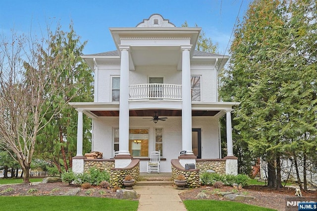 neoclassical / greek revival house featuring covered porch, ceiling fan, a balcony, and stucco siding