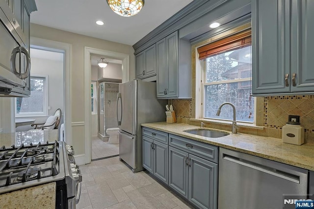 kitchen featuring a sink, stainless steel appliances, gray cabinets, and light stone countertops