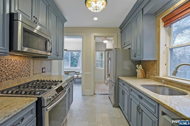 kitchen featuring light stone counters, stainless steel appliances, gray cabinetry, stone finish floor, and a sink