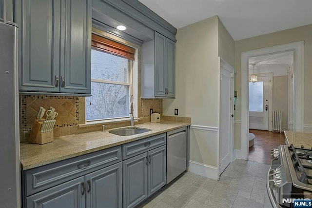 kitchen featuring stainless steel appliances, a sink, baseboards, gray cabinets, and decorative backsplash