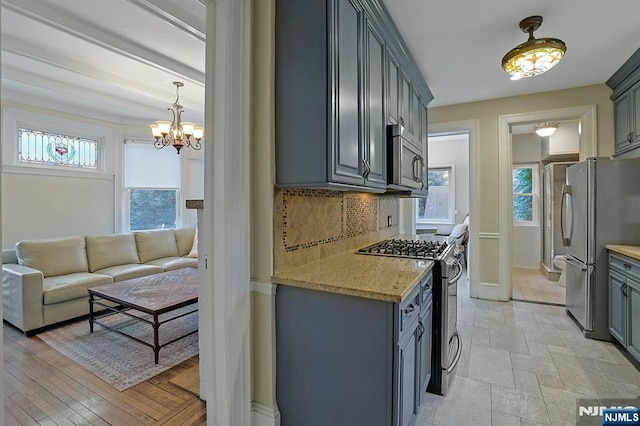 kitchen featuring stainless steel appliances, tasteful backsplash, gray cabinetry, light stone countertops, and plenty of natural light