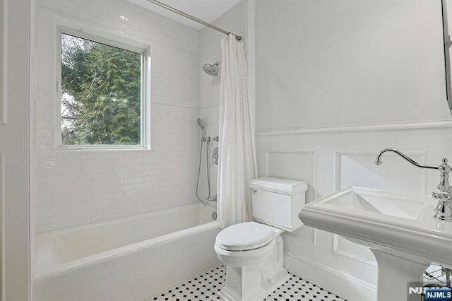 full bath with toilet, shower / bath combo with shower curtain, a sink, and wainscoting