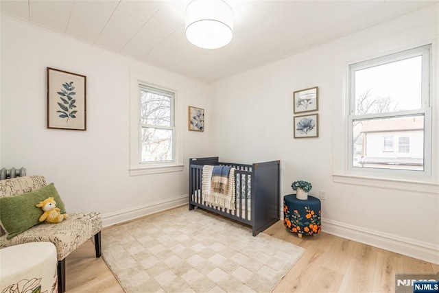 bedroom featuring a nursery area, light wood-style flooring, and baseboards