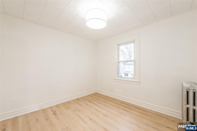 spare room with baseboards, wood finished floors, and radiator