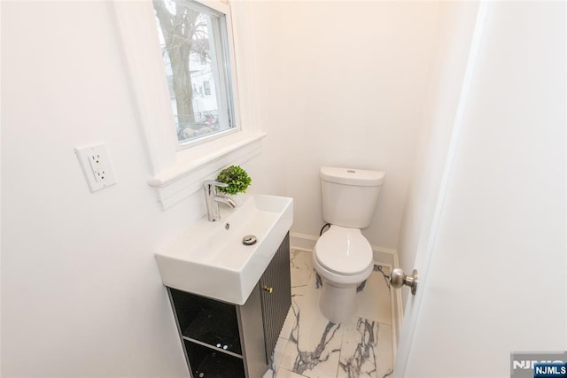 half bathroom featuring toilet, marble finish floor, baseboards, and vanity