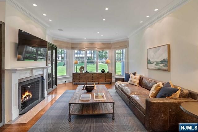 living area featuring a high end fireplace, a wealth of natural light, ornamental molding, and wood finished floors