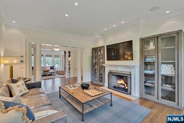 living area with decorative columns, a fireplace with flush hearth, wood finished floors, crown molding, and recessed lighting