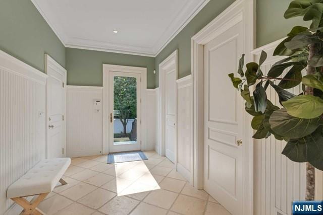 foyer entrance featuring a wainscoted wall, ornamental molding, a decorative wall, and light tile patterned flooring