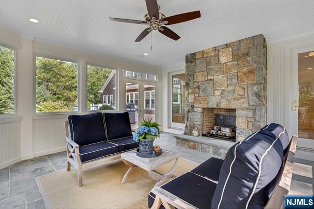 sunroom / solarium featuring a healthy amount of sunlight, a ceiling fan, french doors, and a stone fireplace