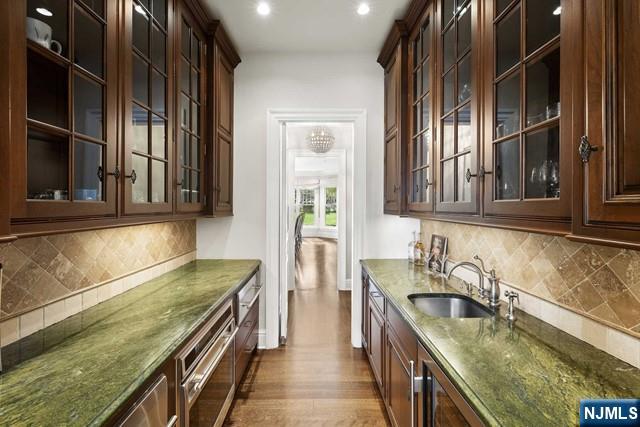 bar with dark wood-style floors, backsplash, stainless steel oven, a sink, and baseboards