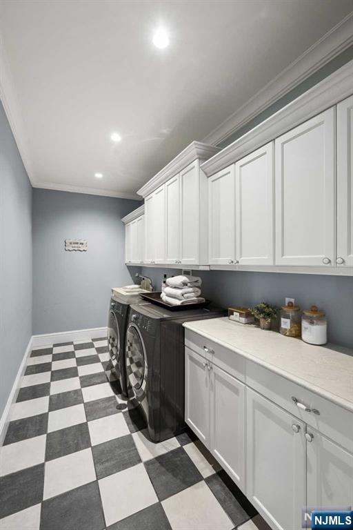 clothes washing area featuring dark floors, ornamental molding, washing machine and dryer, and cabinet space