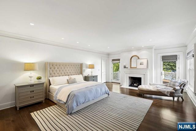 bedroom featuring baseboards, a fireplace with flush hearth, ornamental molding, dark wood-style flooring, and access to outside