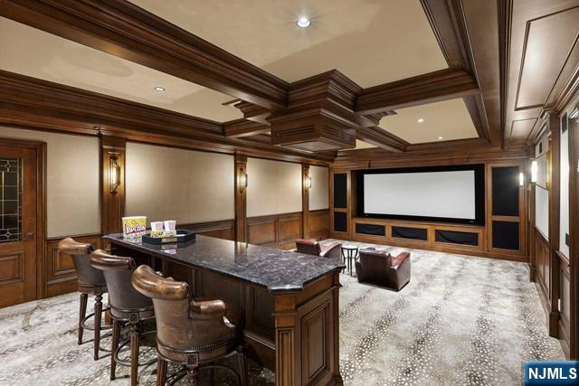 cinema room with coffered ceiling, wainscoting, a dry bar, beamed ceiling, and crown molding