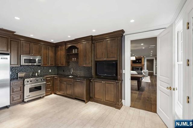 kitchen featuring dark countertops, light wood-style flooring, appliances with stainless steel finishes, open shelves, and backsplash