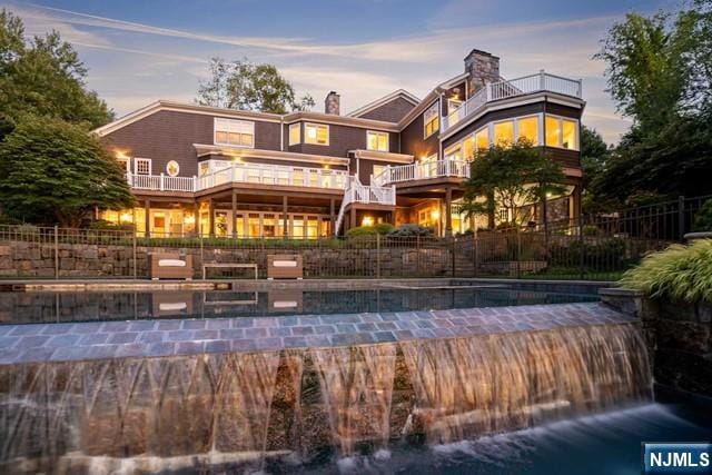 back of property at dusk with a fenced in pool, fence, and a balcony