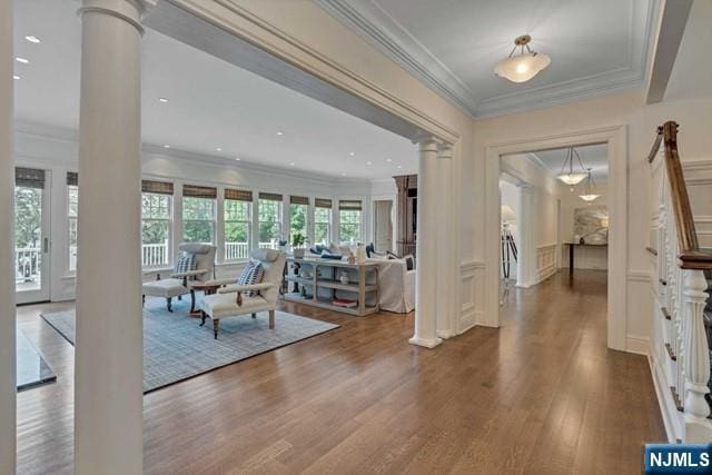 entryway with ornamental molding, decorative columns, a decorative wall, and wood finished floors