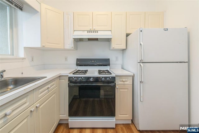 kitchen featuring light countertops, light wood-style flooring, freestanding refrigerator, gas range, and under cabinet range hood