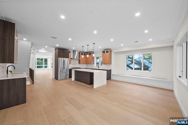 kitchen with high quality fridge, a kitchen island, light countertops, wall chimney range hood, and a sink