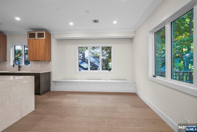 kitchen with light stone counters, light wood-style flooring, a sink, tasteful backsplash, and brown cabinetry