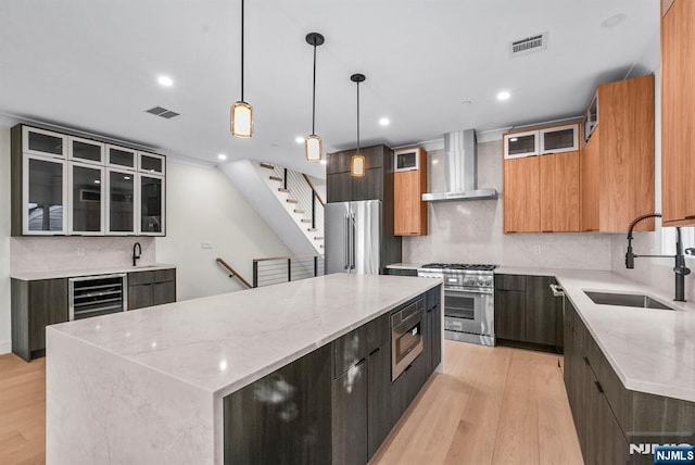 kitchen with a sink, visible vents, a large island, wall chimney exhaust hood, and high end appliances