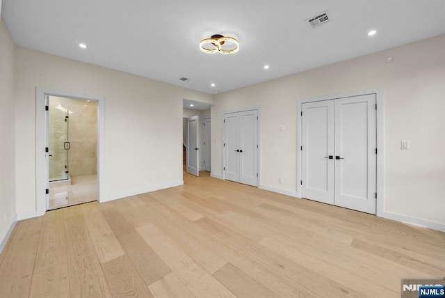 unfurnished bedroom featuring light wood-style floors, visible vents, and two closets