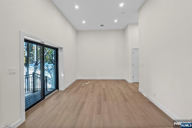 spare room featuring recessed lighting, visible vents, baseboards, a towering ceiling, and light wood-style floors