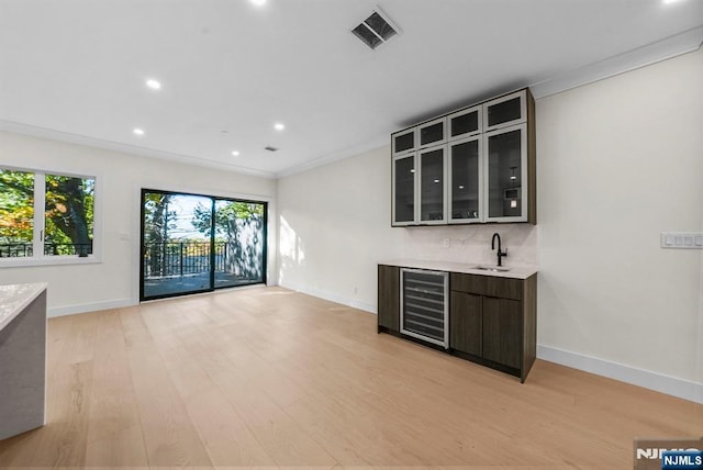 interior space with visible vents, light wood-style flooring, wine cooler, wet bar, and a sink