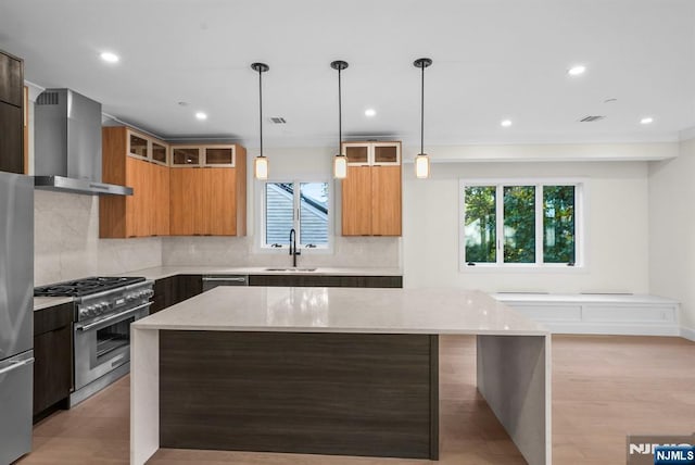 kitchen featuring appliances with stainless steel finishes, a sink, light stone counters, and wall chimney exhaust hood