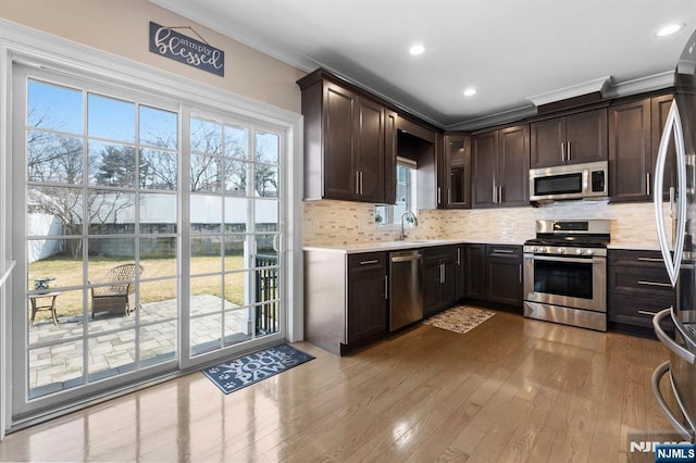 kitchen featuring stainless steel appliances, a sink, dark brown cabinets, light countertops, and backsplash