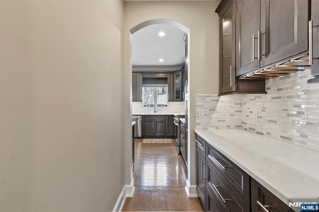 kitchen with appliances with stainless steel finishes, arched walkways, dark brown cabinets, and dark wood-type flooring